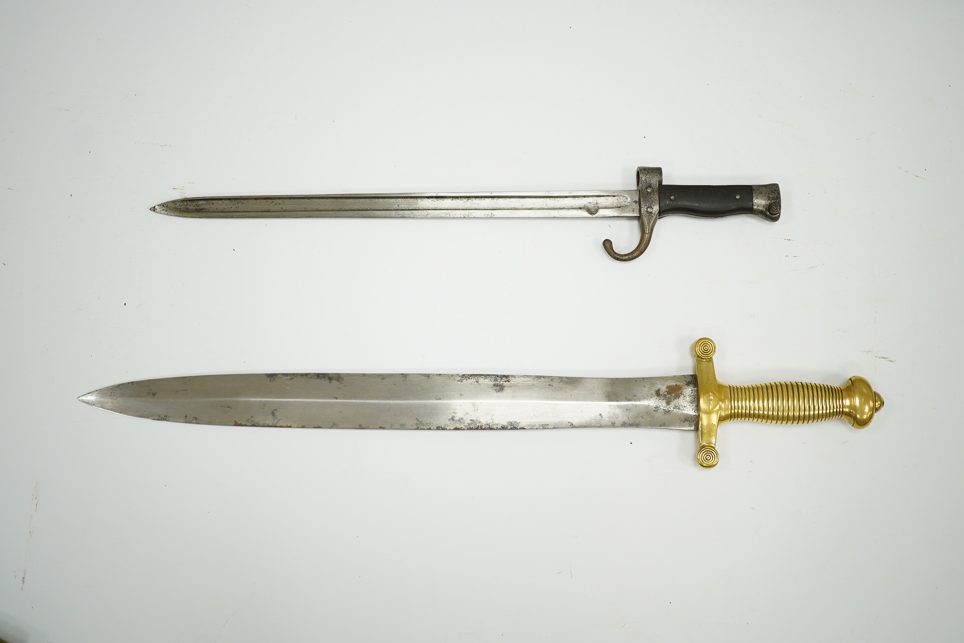 A 19th century French infantryman’s sidearm Gladius with swollen double edged blade, and regulation cast brass cruciform hilt, in its brass mounted leather scabbard, together with a continental bayonet also in scabbard.